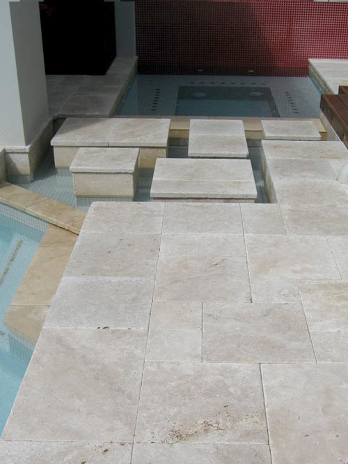 Travertine Linen tumbled unfilled stone tiles and coping around swimming pool with feature steps and spa