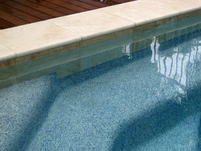 Closeup of Travertine Linen Stone Coping and waterline tiles