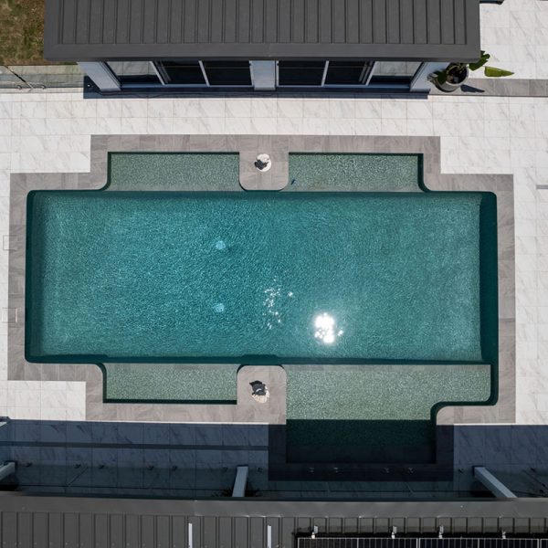 Overhead view of large, fully-tiled pool with CMC560 Ubud Green Wavy 23mm ceramic mosaic tile, Cosmos porcelain coping edge and Carrara Marblano pool surrounds